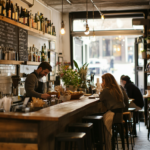 A cozy, independent restaurant thriving in tough economic times. A warm, inviting atmosphere with happy diners enjoying meals, while a digital menu and automated ordering system enhance efficiency. In the background, a chef and owner confidently manage the restaurant, symbolizing resilience and success. A chalkboard sign reads ‘Thriving Local Business’ outside the entrance.
